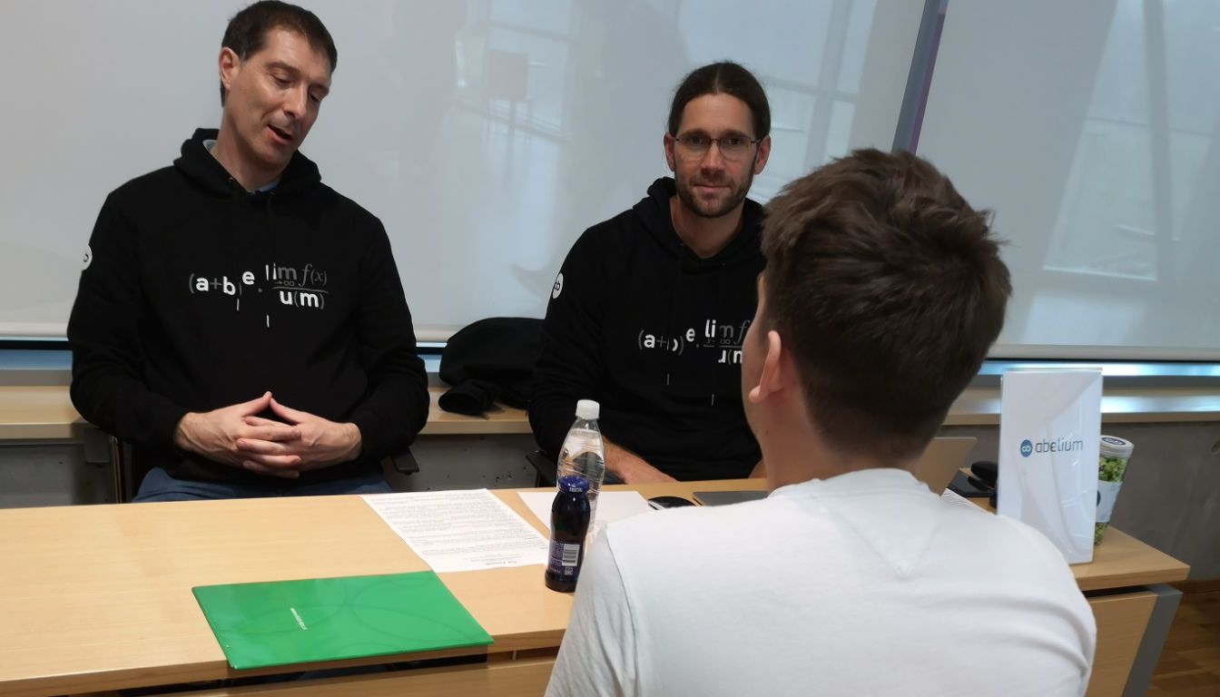 Two Abelium colleagues talking with a student across a desk during career interviews at Data Science Career Day